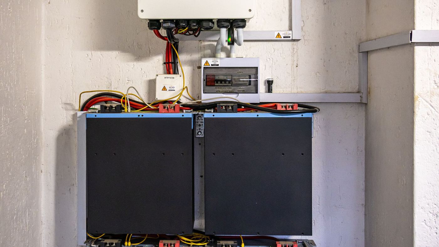 A wall-mounted inverter and battery stack in a domestic utility cupboard