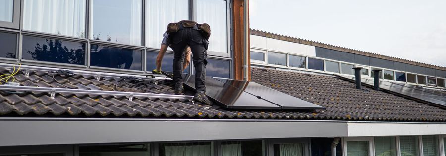 A technician working on a flat-roof solar array with housing behind